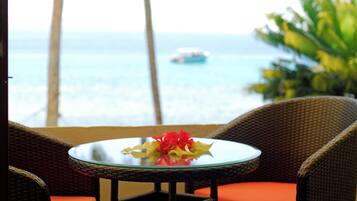 A wicker chair with an orange cushion, a small glass table with a flower arrangement, and a view of the ocean with a boat in the distance.