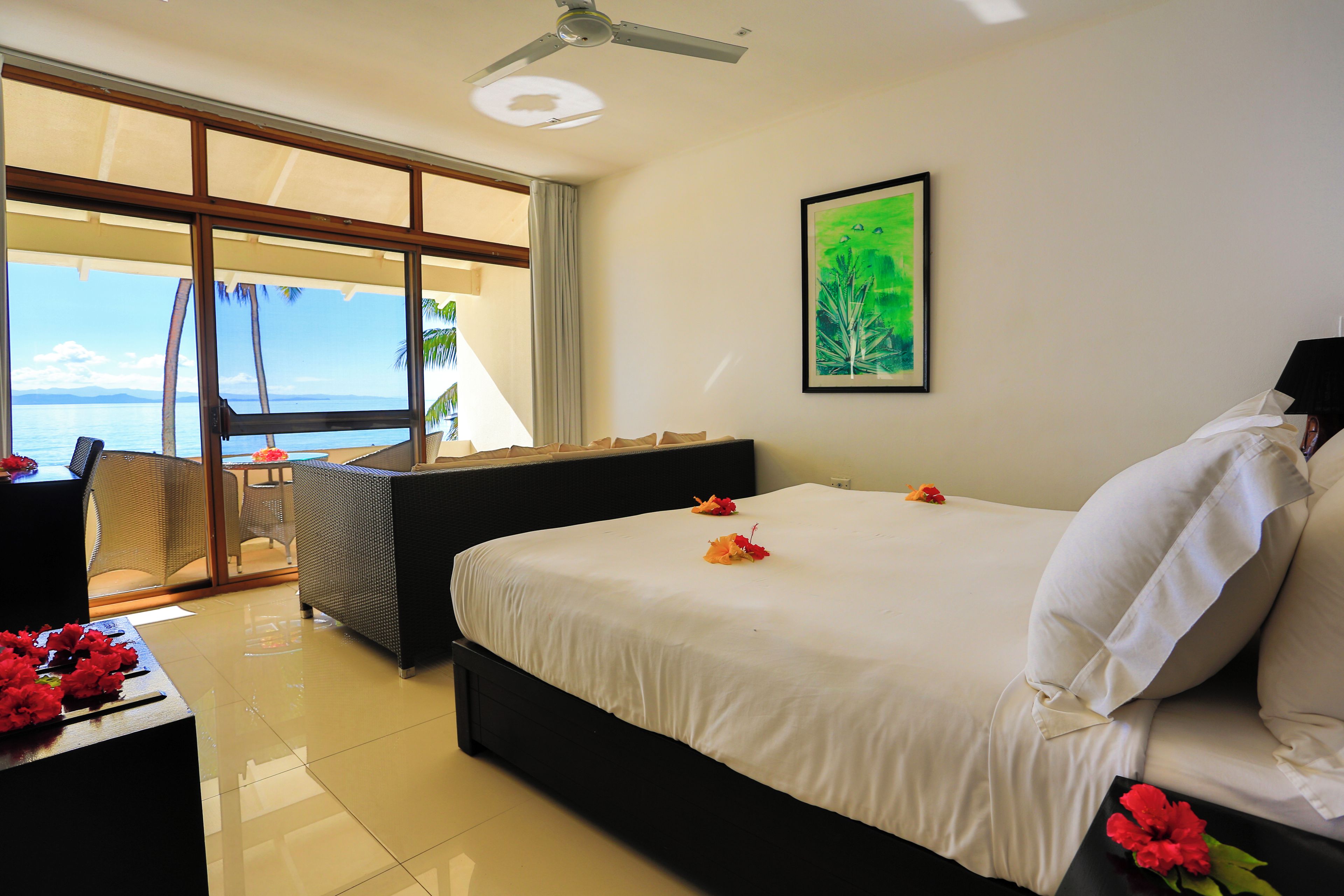 A hotel room with a bed, a chair, a table, and a view of the sea.