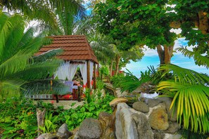 A small, rustic hut with a tiled roof, surrounded by lush greenery and a small water feature. - Garden Island Resort (Taveuni Island East)