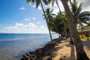 A beach with palm trees, a stone wall, and a building with a balcony. - Garden Island Resort (Taveuni Island East)