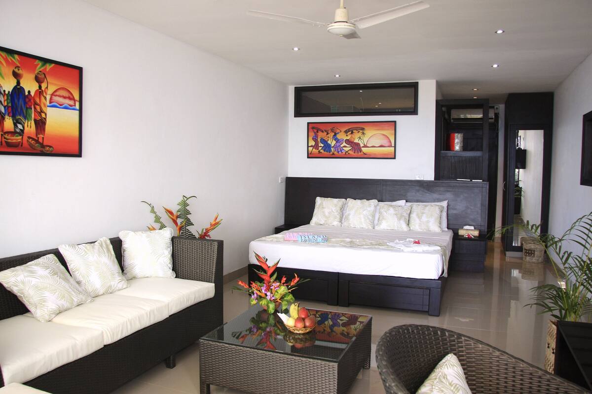 Une chambre d’hôtel moderne, dotée d’un grand lit, d’un canapé, d’une table basse agrémentée d’un arrangement floral et de deux tableaux aux murs.