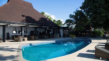 A swimming pool with a curved edge, surrounded by a covered patio area with outdoor furniture.