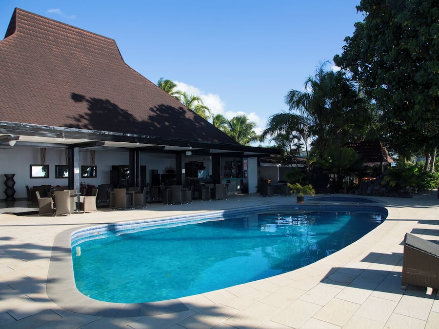 Una piscina de borde curvo, rodeada por un patio cubierto con mobiliario exterior.