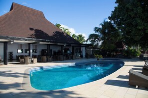 A swimming pool with a curved edge, surrounded by a covered patio area with outdoor furniture. - Garden Island Resort (Taveuni Island East)