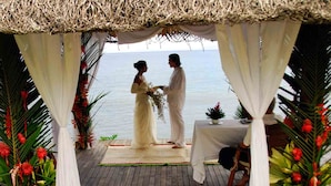Una pareja parada bajo un techo de paja con vistas al mar.