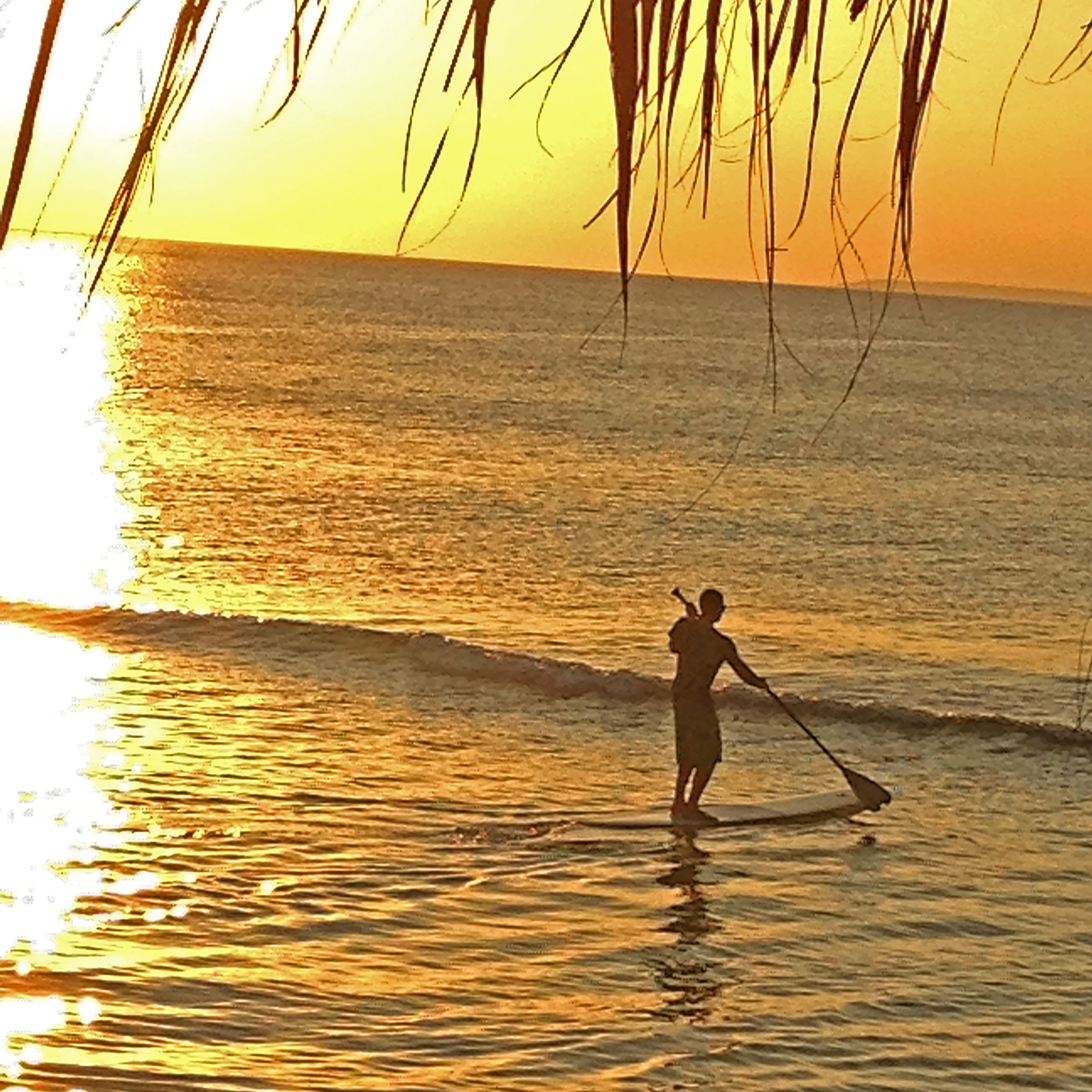 A person paddleboarding on calm waters during sunset.