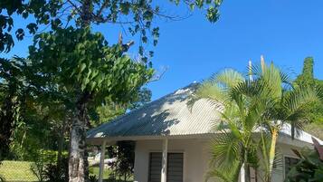 A small, single-story building with a corrugated metal roof, surrounded by lush greenery and a clear blue sky.