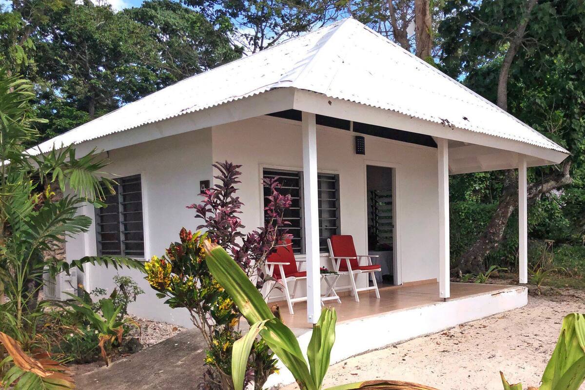 A white building with a covered porch and red chairs.
