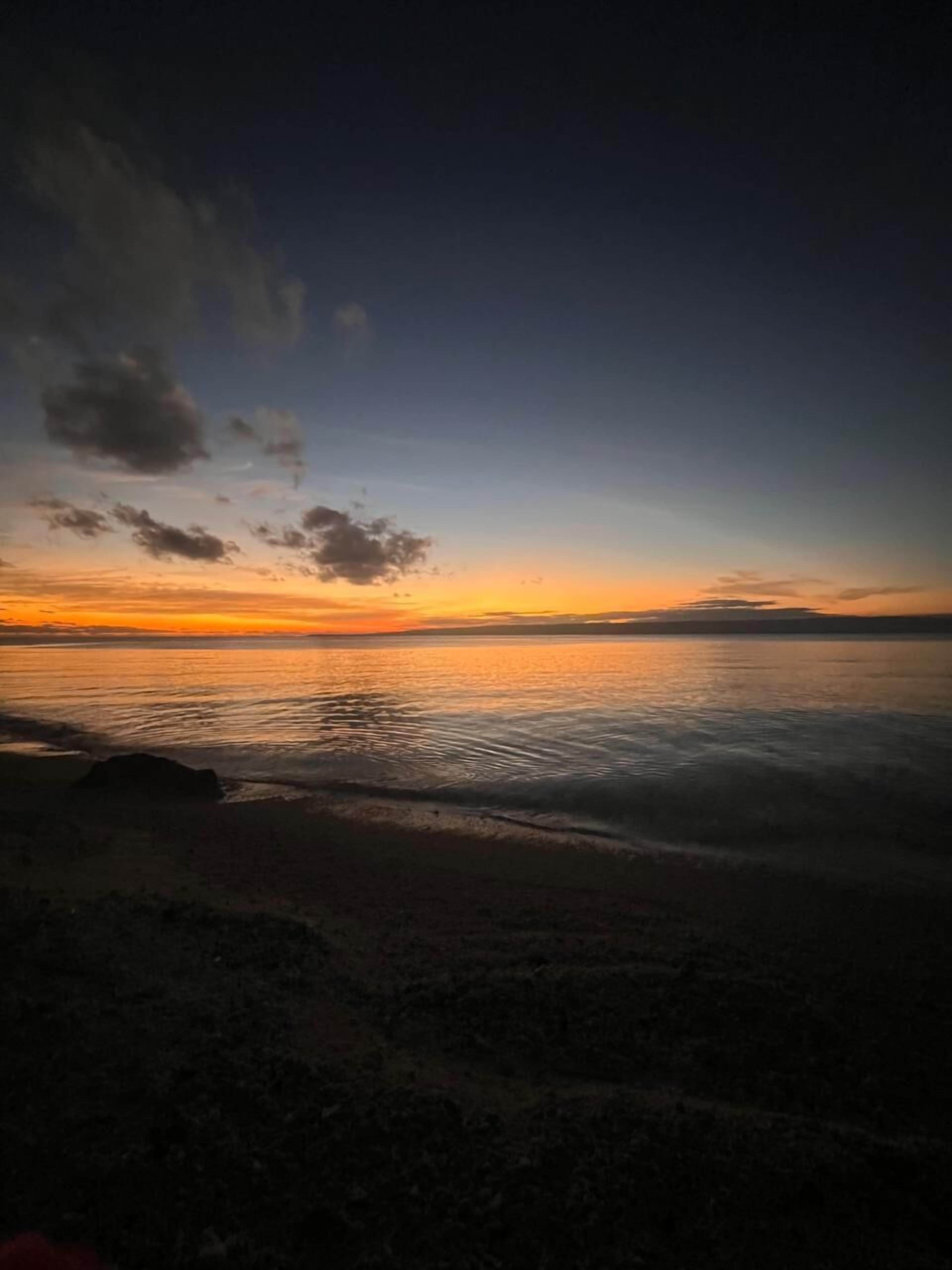Escena de playa con un atardecer sobre el agua.