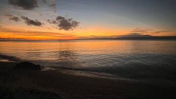 Escena de playa con un atardecer sobre el agua.