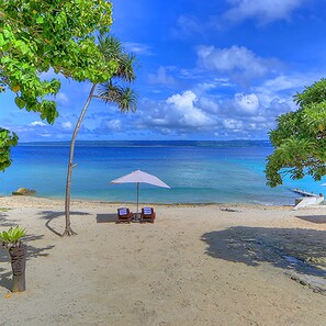 A beach with two lounge chairs under a beach umbrella, a palm tree, and clear blue water. - Coco Beach Resort (Port Vila)