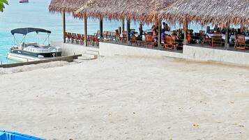 Una playa con sombrillas de paja y sillas reclinables, un bote anclado en la arena y una vista despejada del mar.