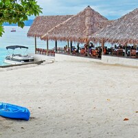 Una playa con sombrillas de paja y sillas reclinables, un bote anclado en la arena y una vista despejada del mar.