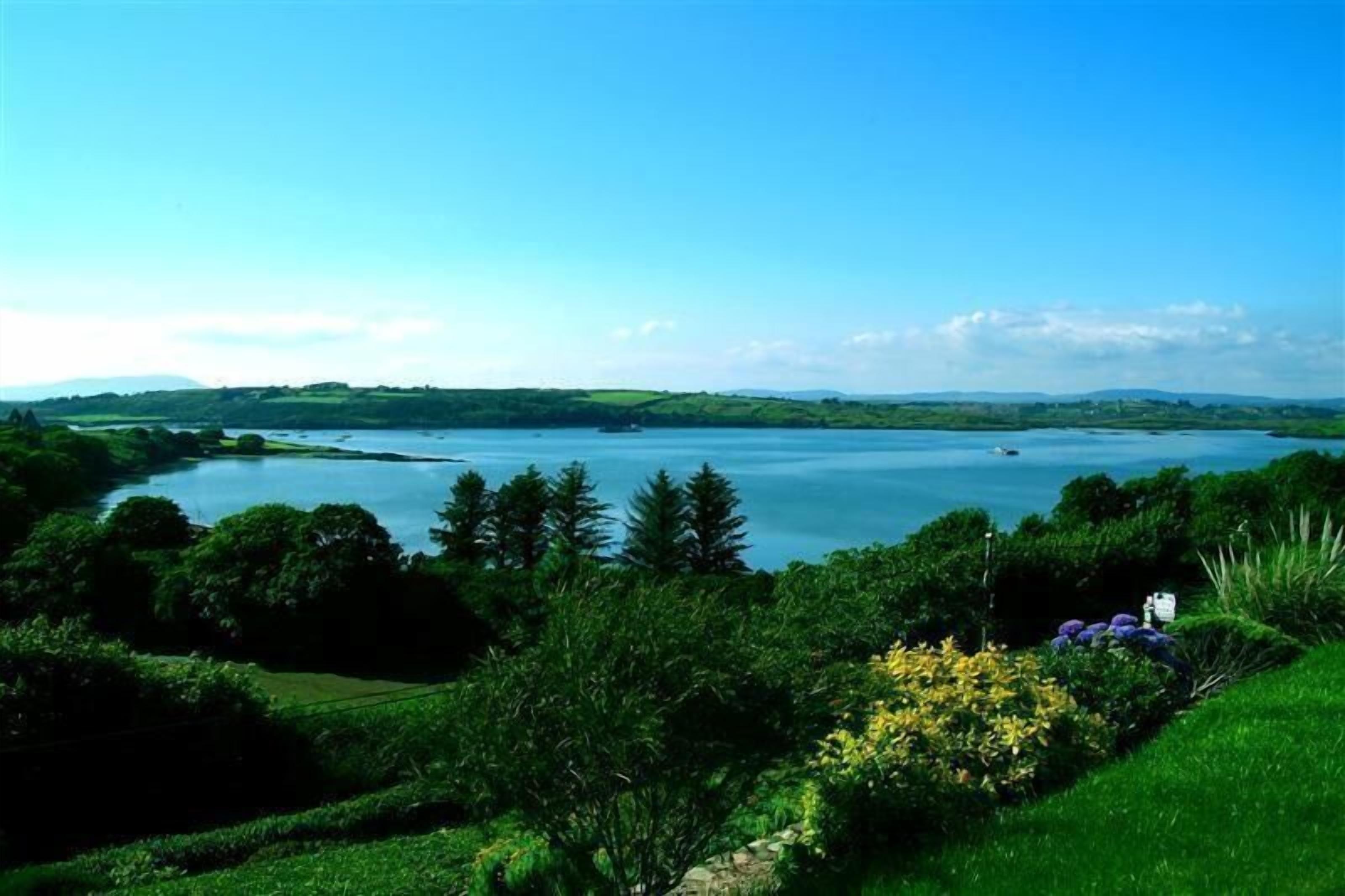 A lakeside view with a boat, greenery, and distant hills.