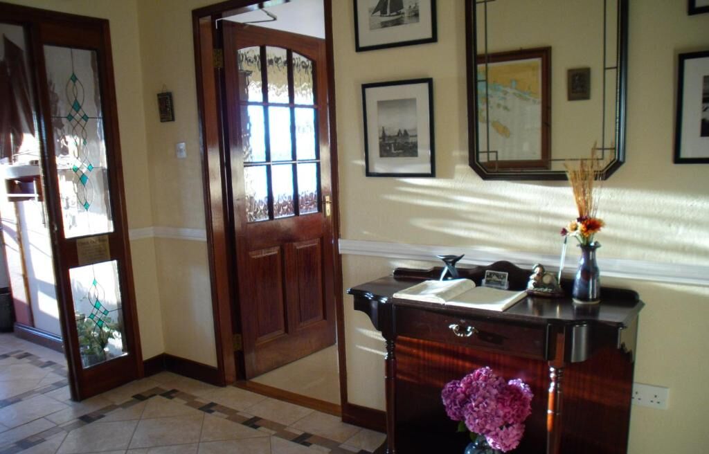 A hallway with a wooden door, a desk with a vase of flowers, and framed pictures on the wall.