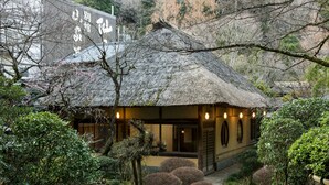 A traditional Japanese-style building with a thatched roof, surrounded by well-maintained gardens and a stone pathway.