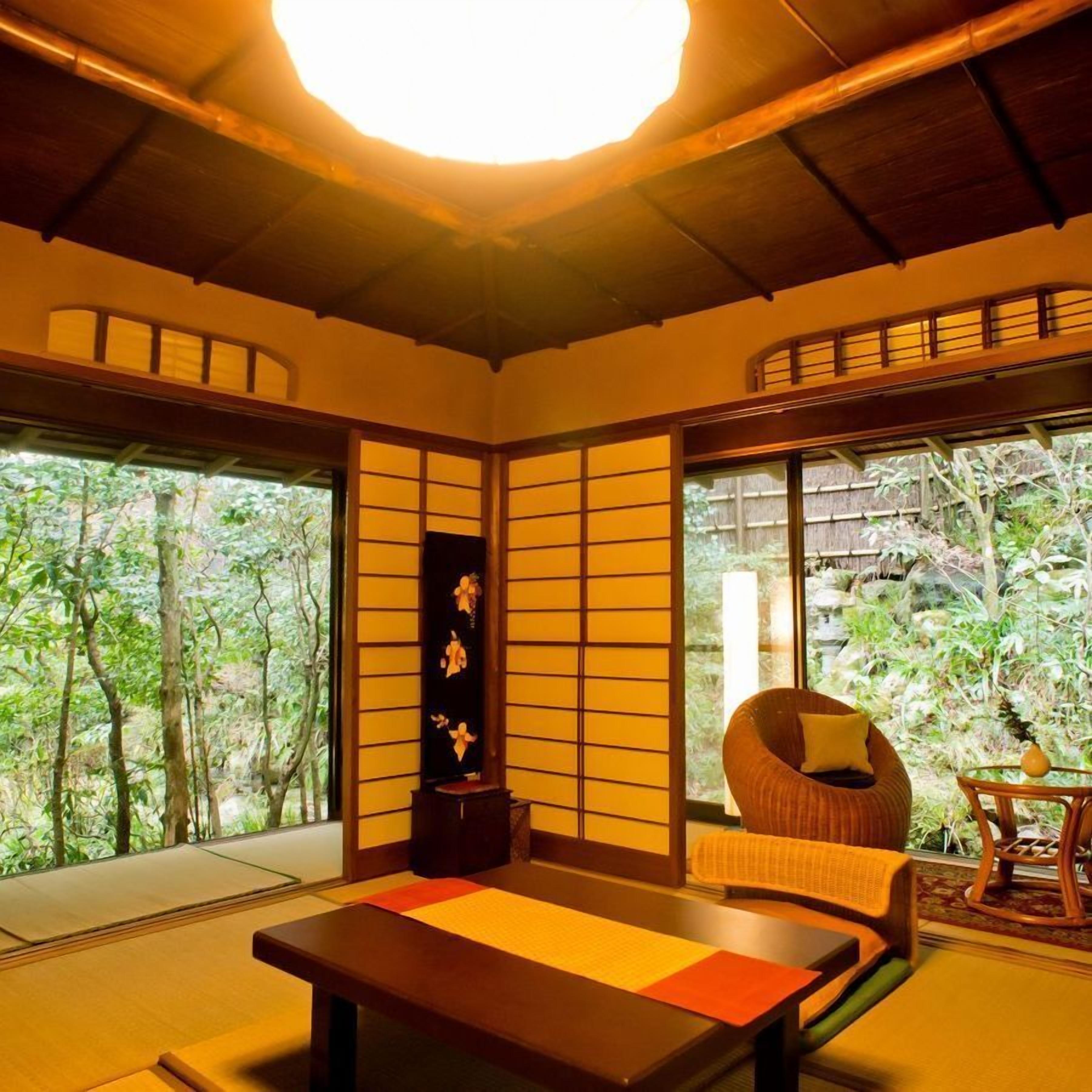 A traditional Japanese room with tatami flooring, a low table, a cushioned seating area, and a sliding door leading to a garden.