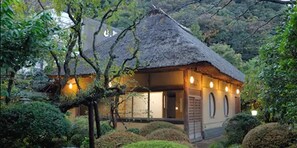 A traditional thatched-roof house with a wooden exterior, surrounded by lush greenery. - Yamagaso (Hakone)