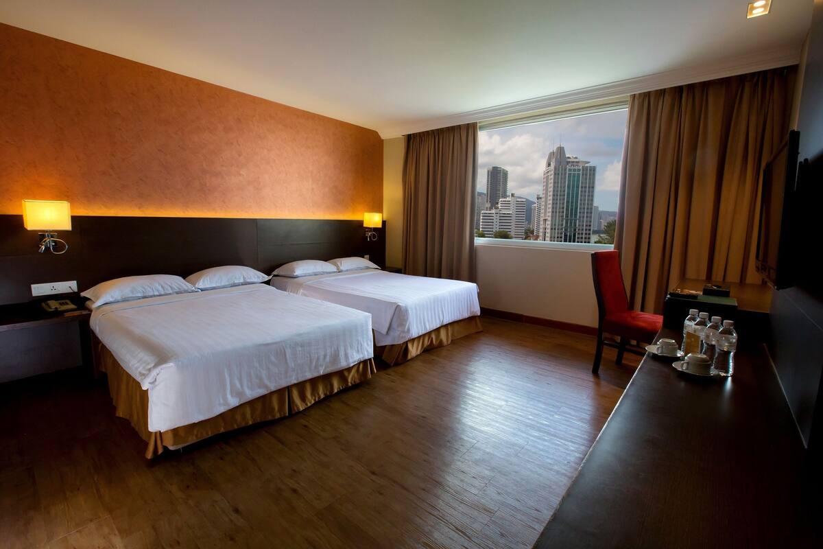 A hotel room with two beds, a wooden floor, a city view, a TV, and a small table with items.