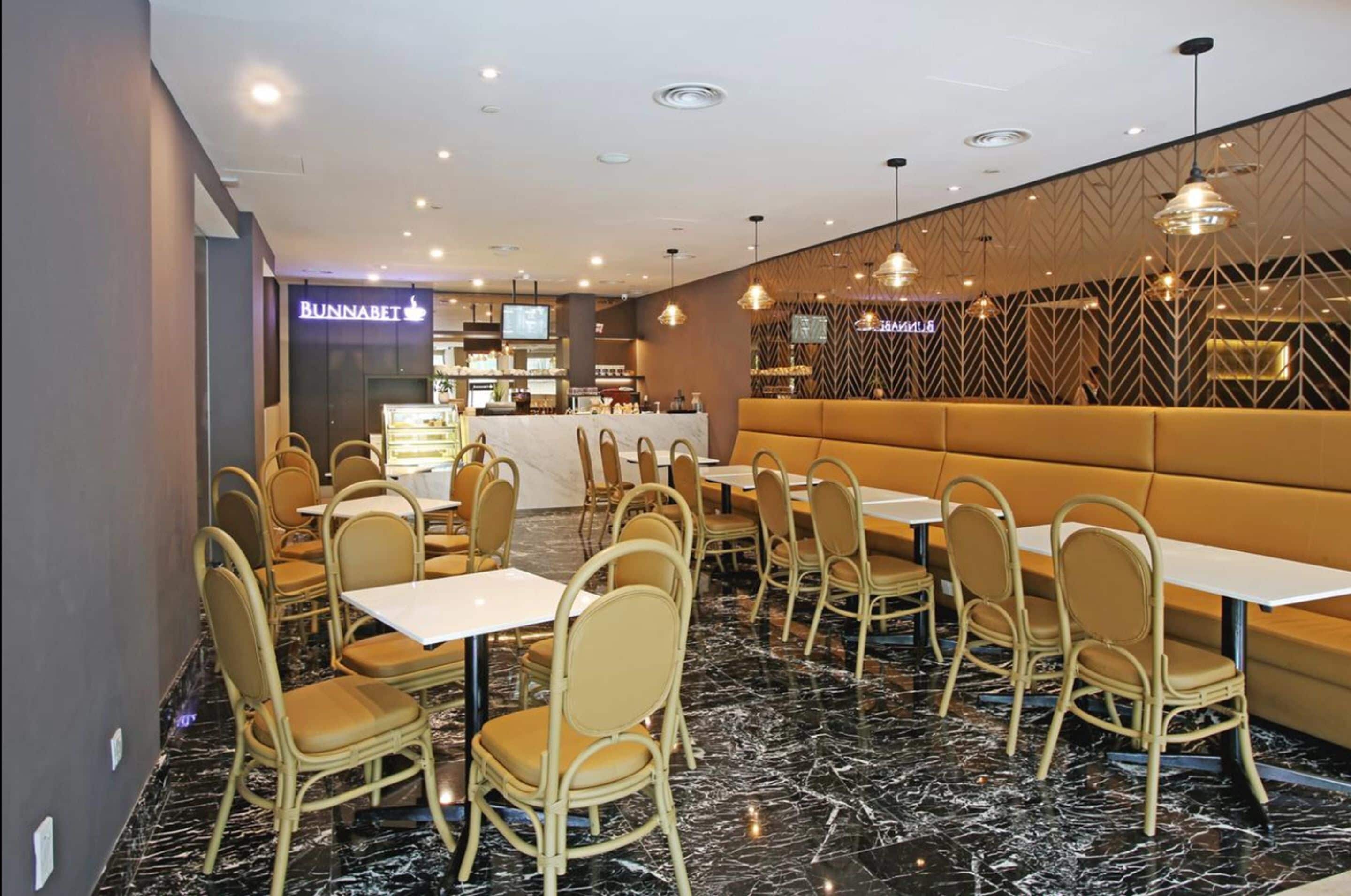 Un restaurante con suelo de mármol, asientos tapizados en amarillo y sillas de metal.