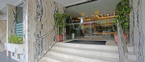 A hotel entrance with marble steps, glass doors, and potted plants.