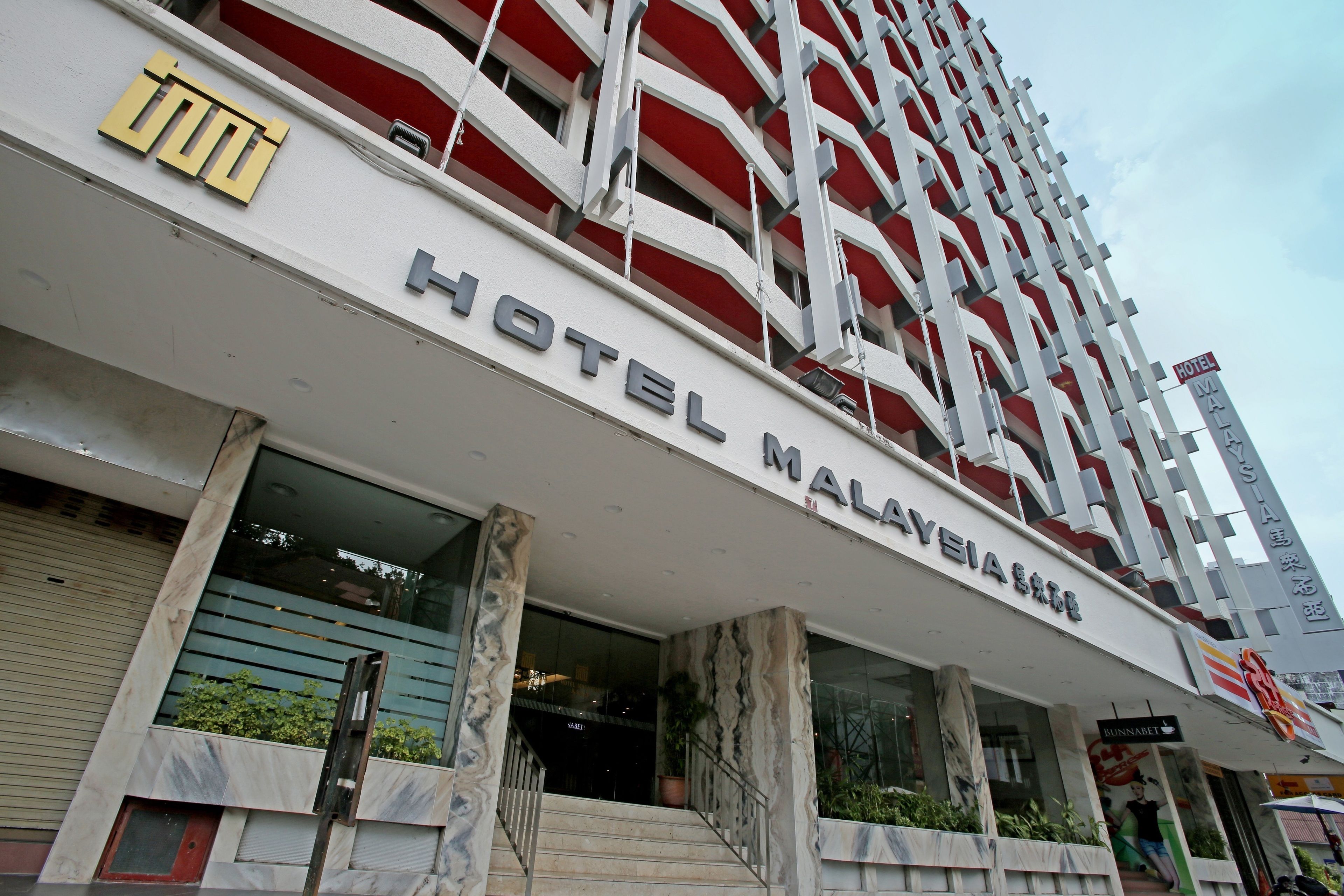 A hotel with a modern facade, a prominent sign reading "HOTEL MALAYSIA," and a staircase leading to the entrance.