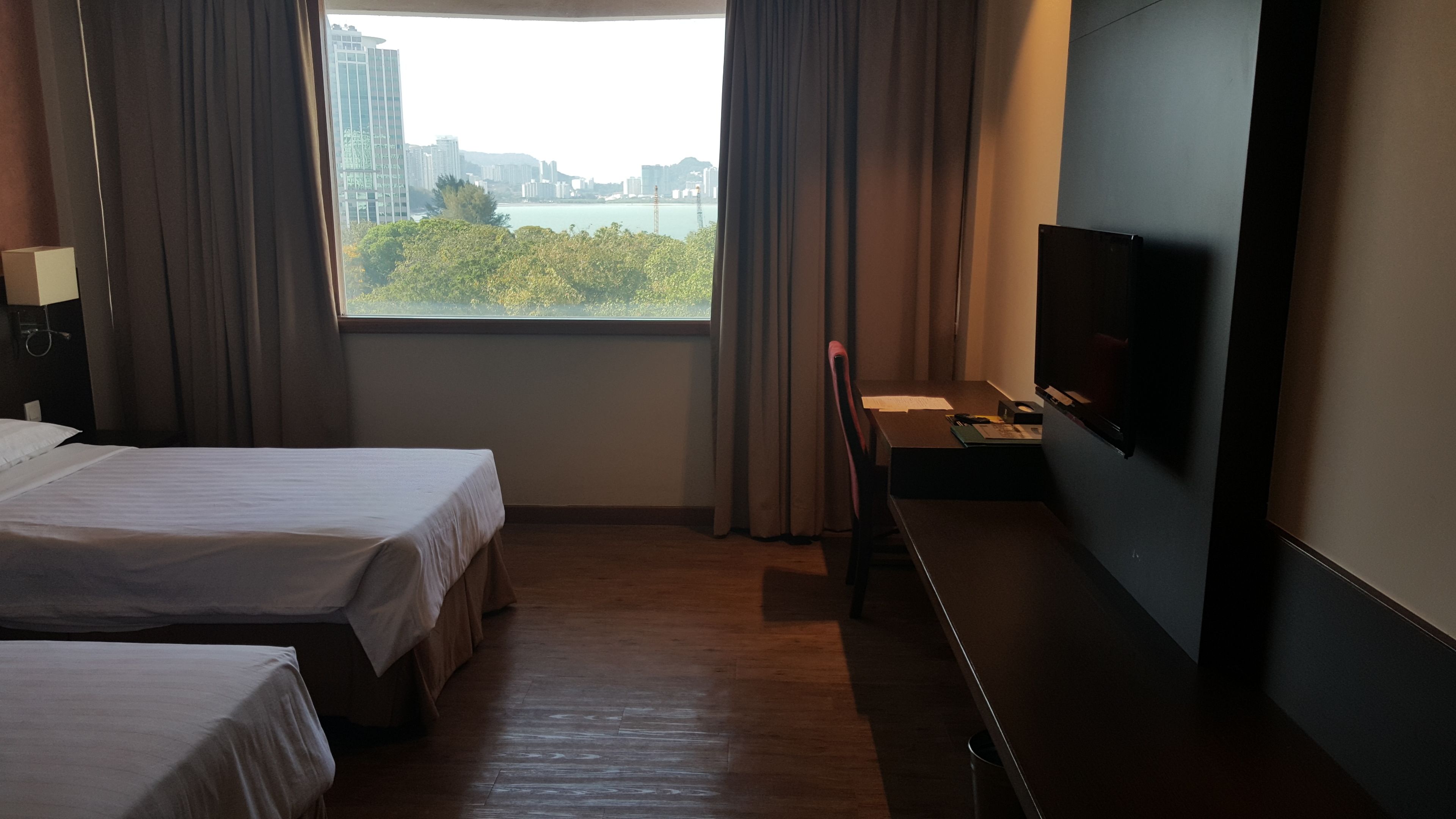 Een hotelkamer met twee bedden, een bureau, een televisie en een raam met uitzicht op de stad.