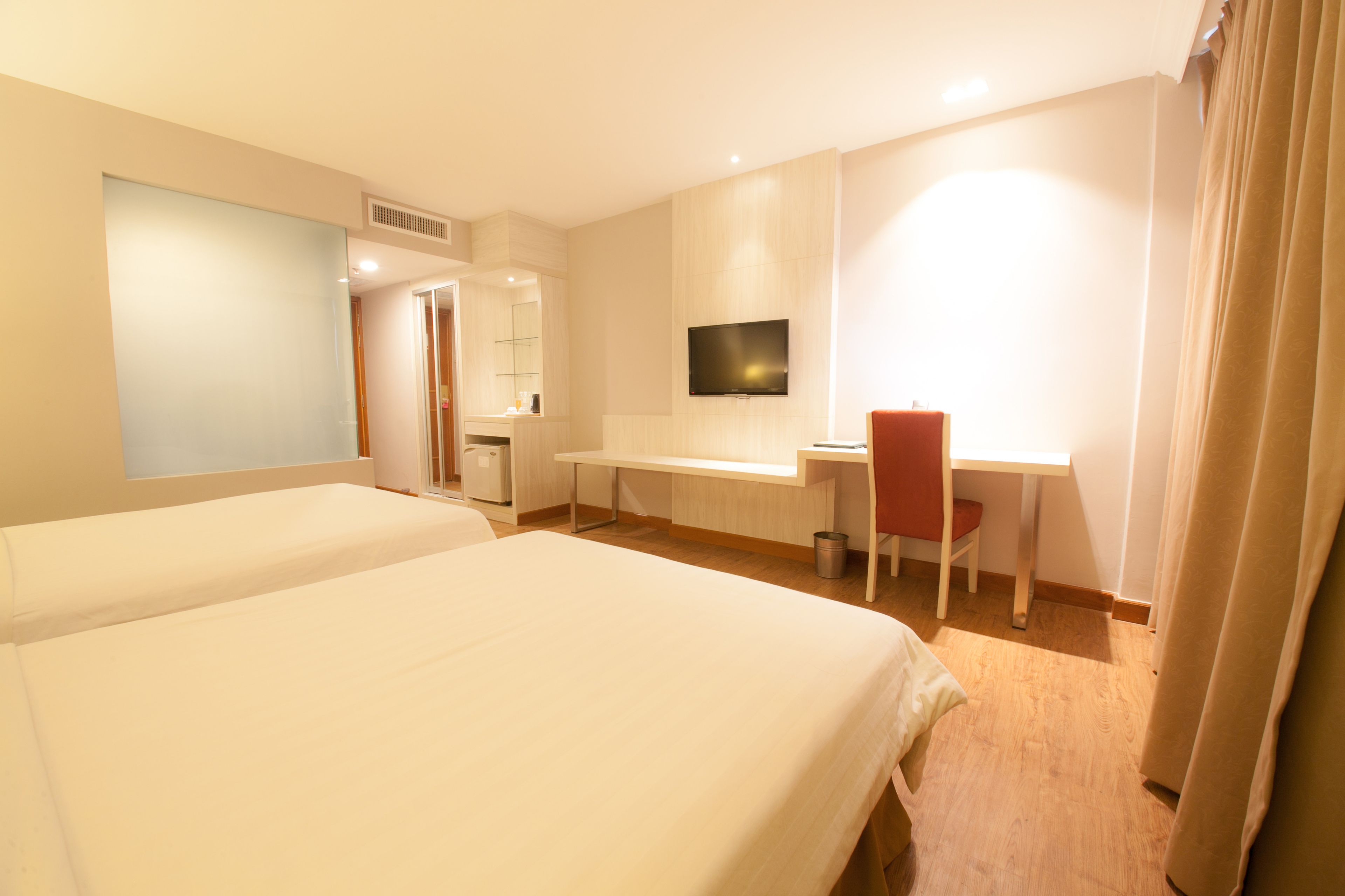 A hotel room with two beds, a desk, a chair, a television, and a bathroom.