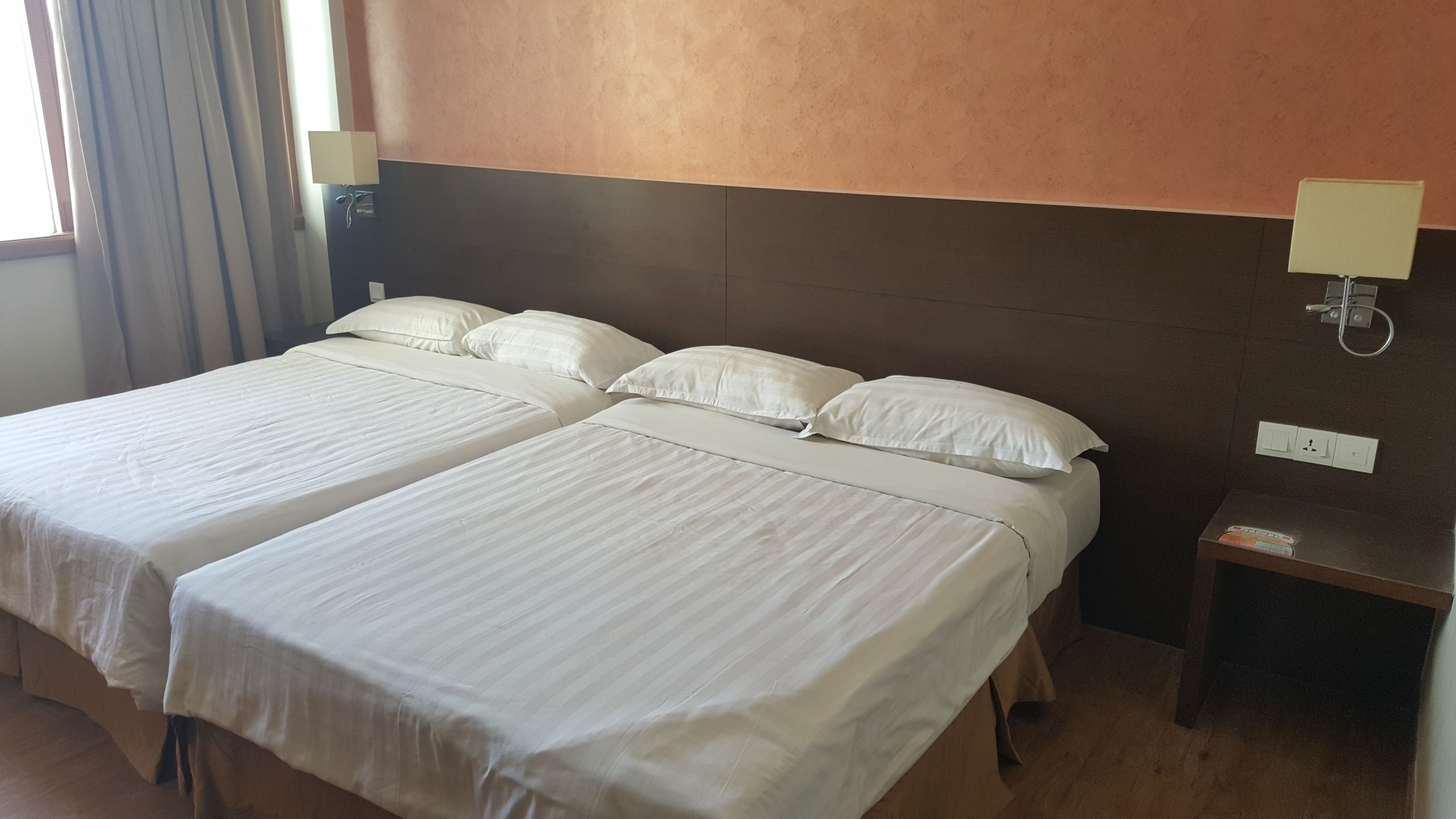 A hotel room with two beds, a nightstand, and a wall-mounted lamp.