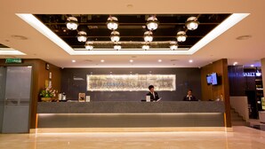 Et hotellets reception område med et moderne design, med en marmor disk, et stort abstrakt maleri på væggen og et digitalt skærm der viser information.
