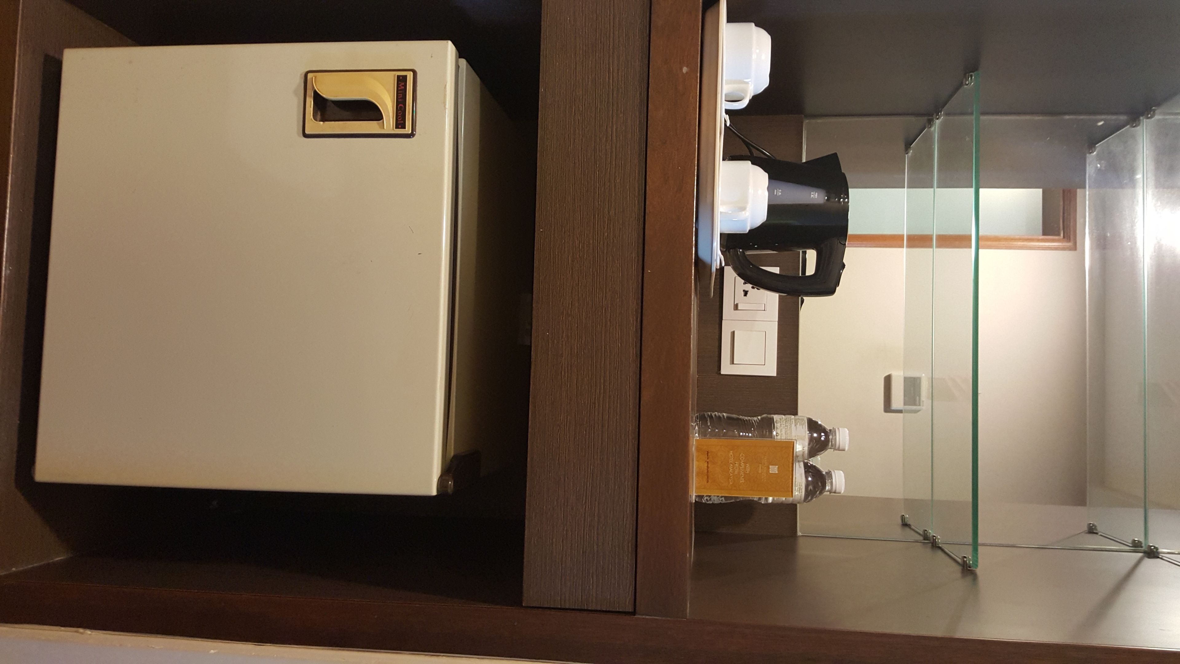 A compact refrigerator with a handle, a glass partition, and a small table with a bottle and a box.