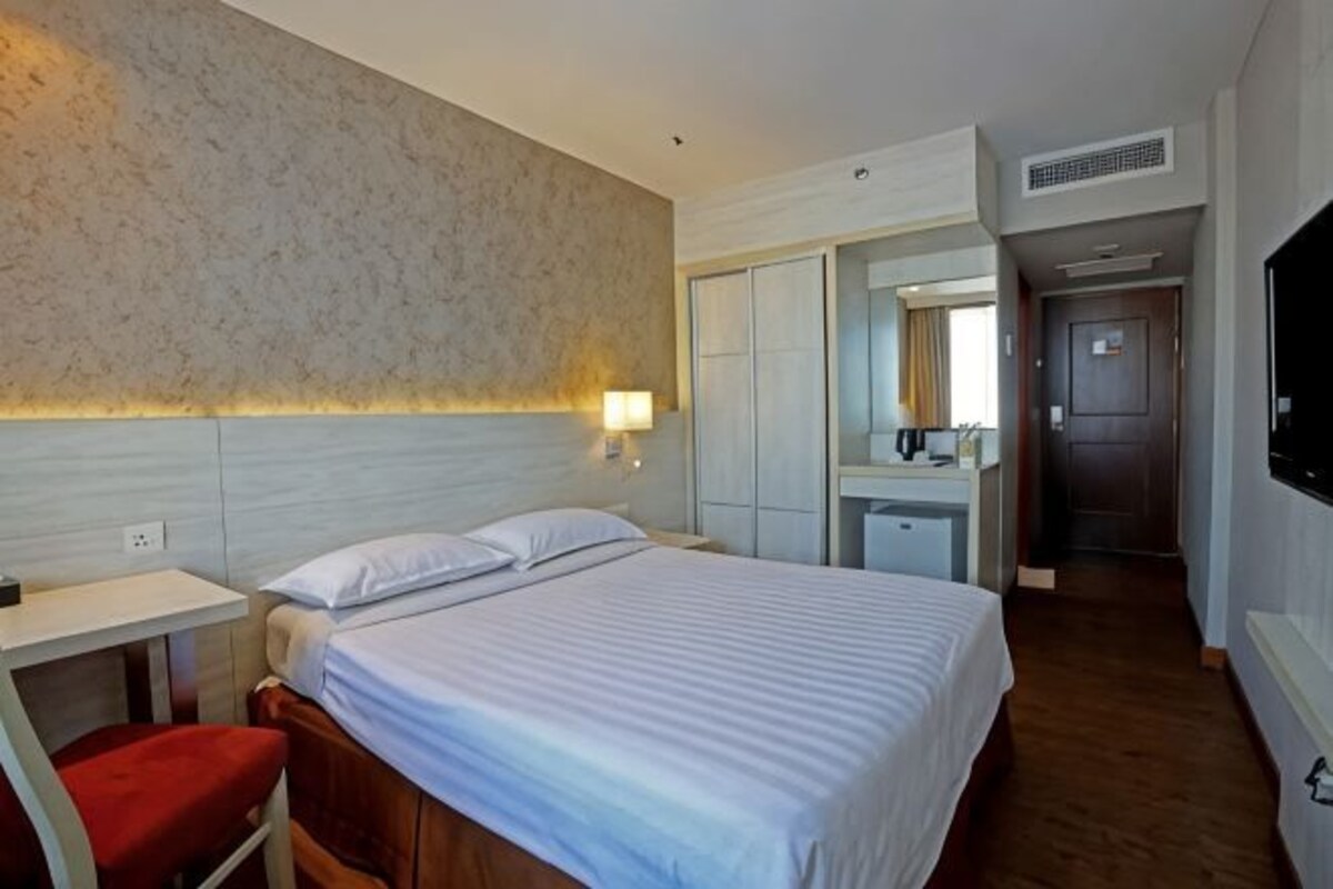 A hotel room with a bed, a desk, a chair, a mirror, and a television.