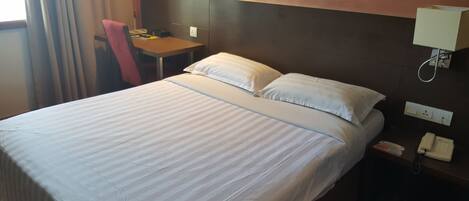 A hotel room with a bed, a desk, a chair, a lamp, and a phone on the nightstand.