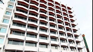 Et hotel med flere etager og balkoner, et skilt med teksten "HOTEL MALAYSIA 6258", samt et gades billede med køretøjer og en cykel.
