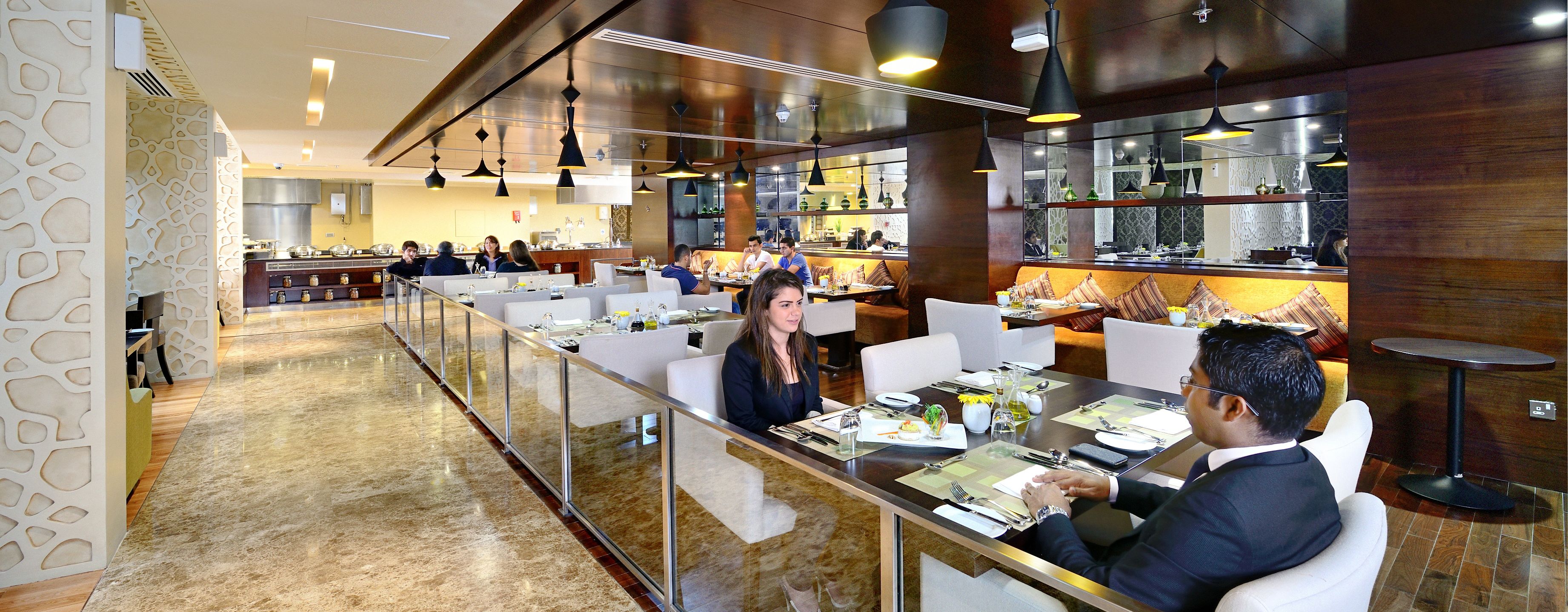 Um restaurante moderno com um balcão extenso, várias mesas e uma cozinha ao fundo.