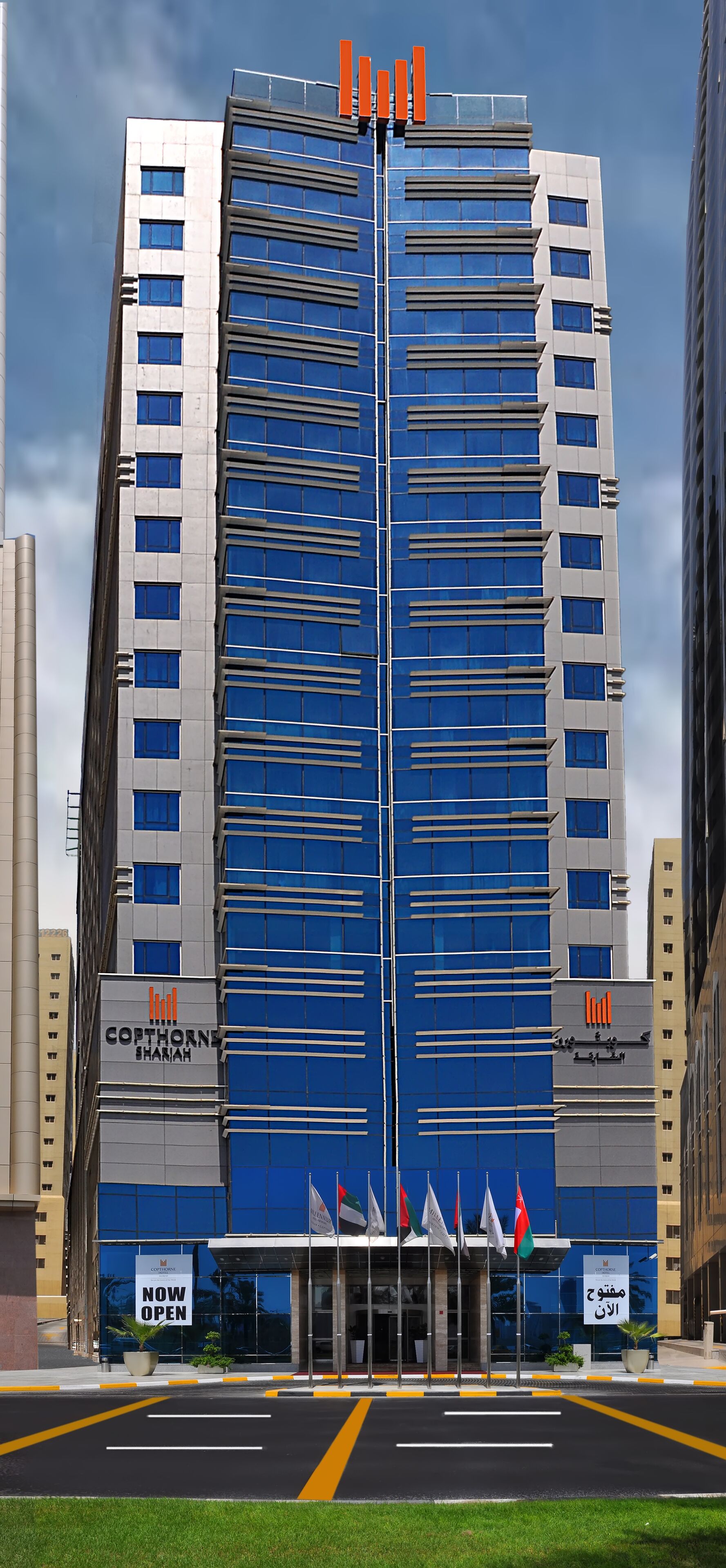 A modern hotel building with a prominent blue facade, multiple floors, and a central entrance with flags.