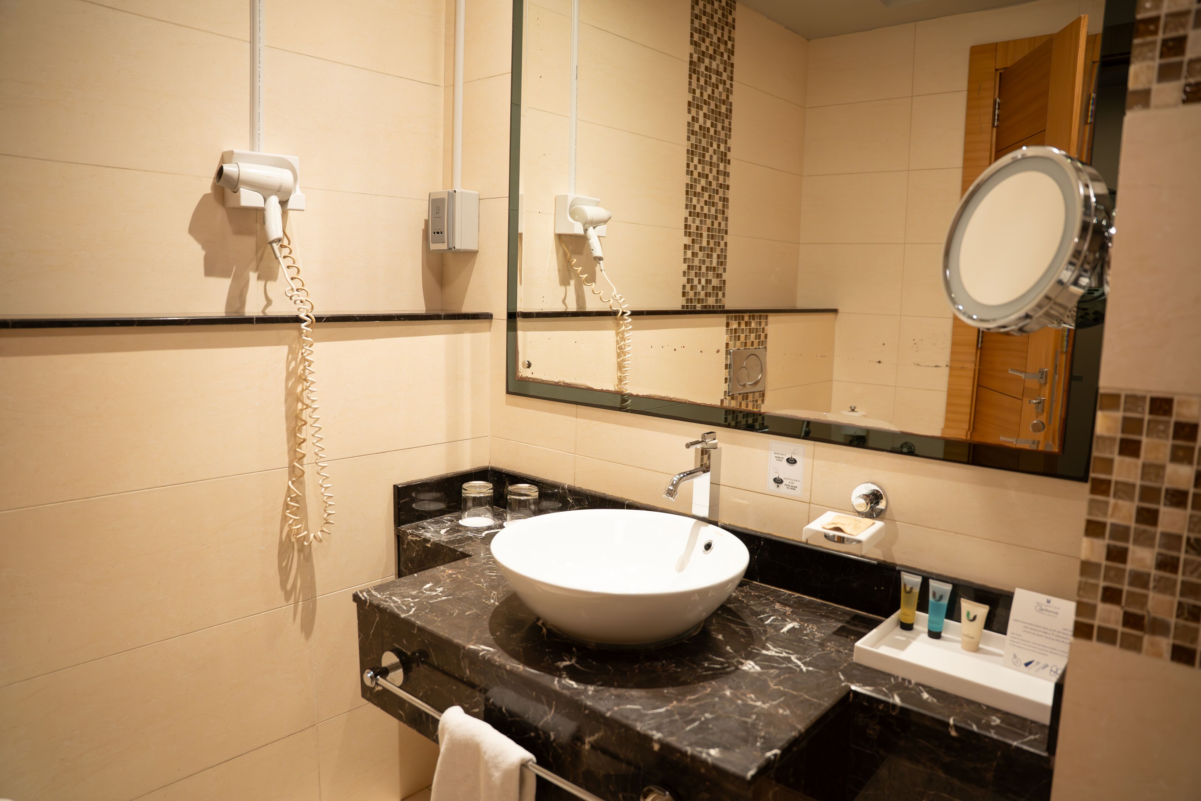 A bathroom with a marble sink, a mirror, and a hairdryer mounted on the wall.