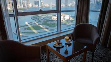 A hotel room with a large window offering a view of a city skyline and a body of water. There is a table with a plate of food and a glass of orange juice.
