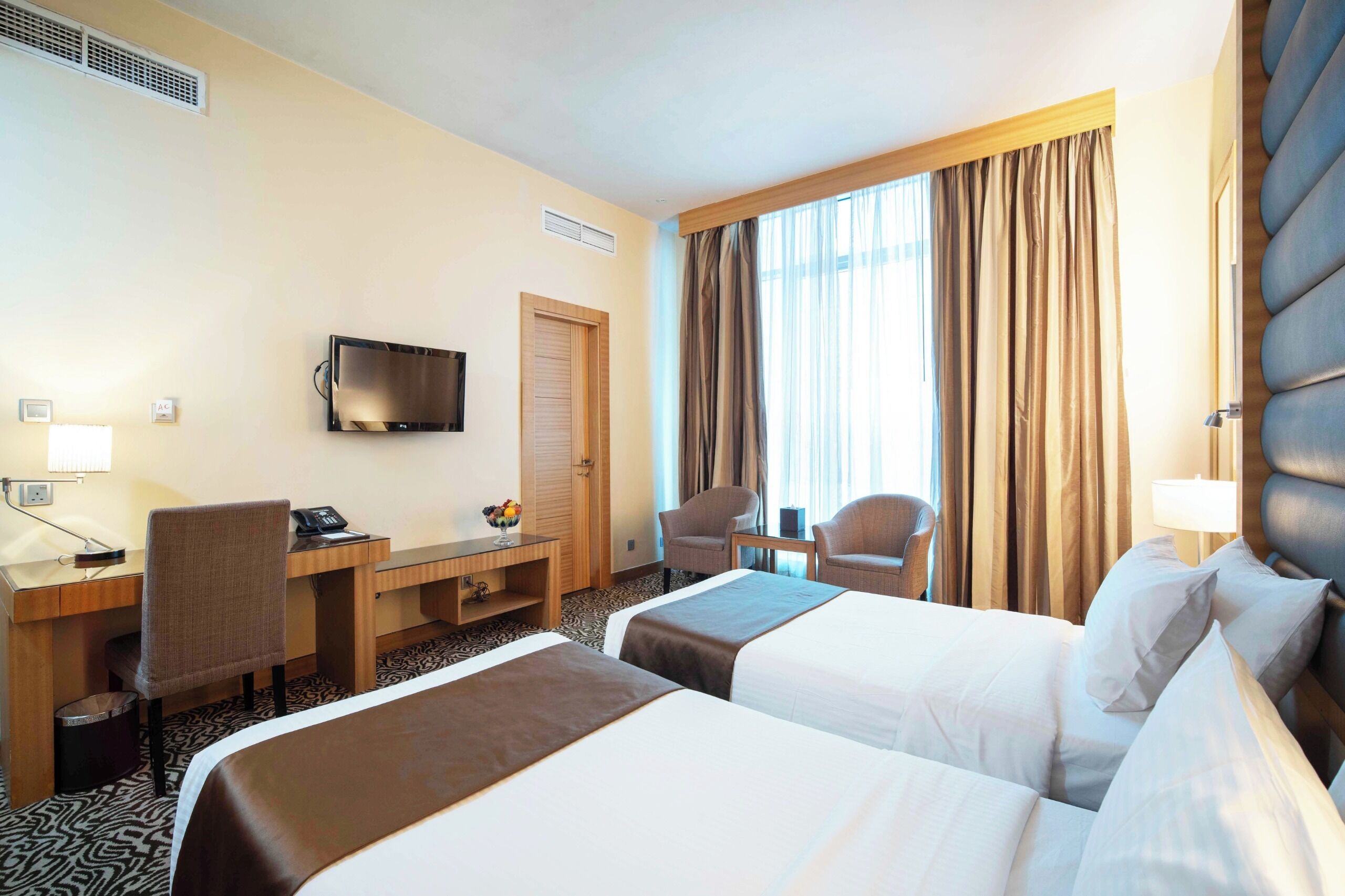 A hotel room with two beds, a desk with a chair, a television, and a window with curtains.