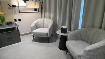 Ein modernes Zimmer mit zwei Sesseln, einem kleinen Tisch mit Taschentuchbox, einer Lampe und einem Schreibtisch mit Blumenvase.