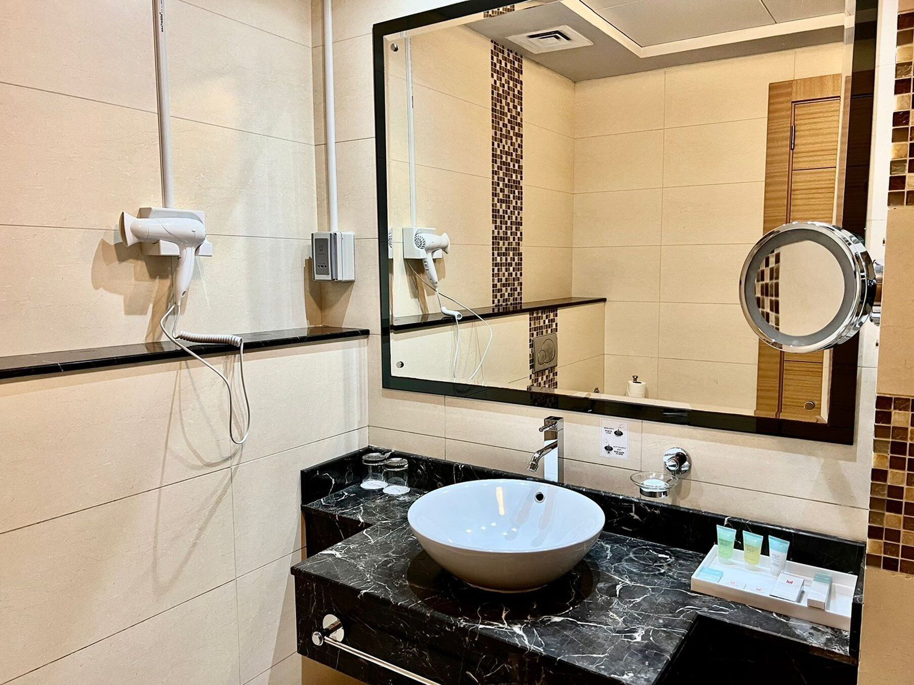 A bathroom with a white sink, black marble countertop, and a mirror with a round frame.