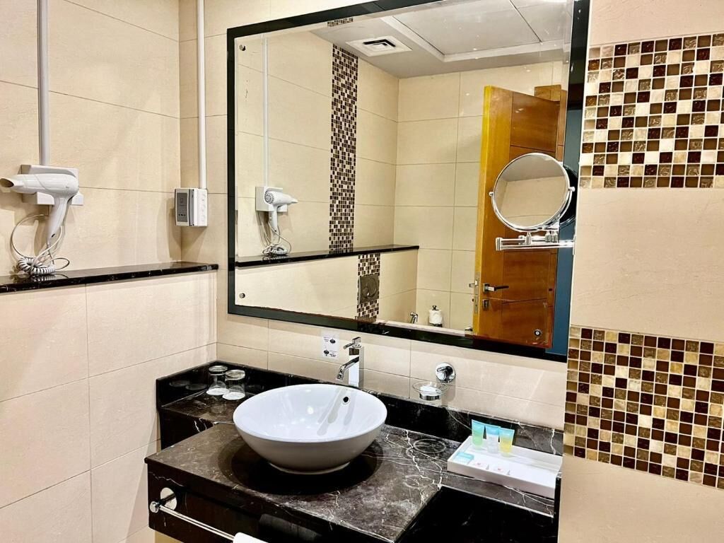 Une salle de bain dotée d’un grand miroir, d’un lavabo avec un plan de travail en marbre et d’un sèche-cheveux fixé au mur.