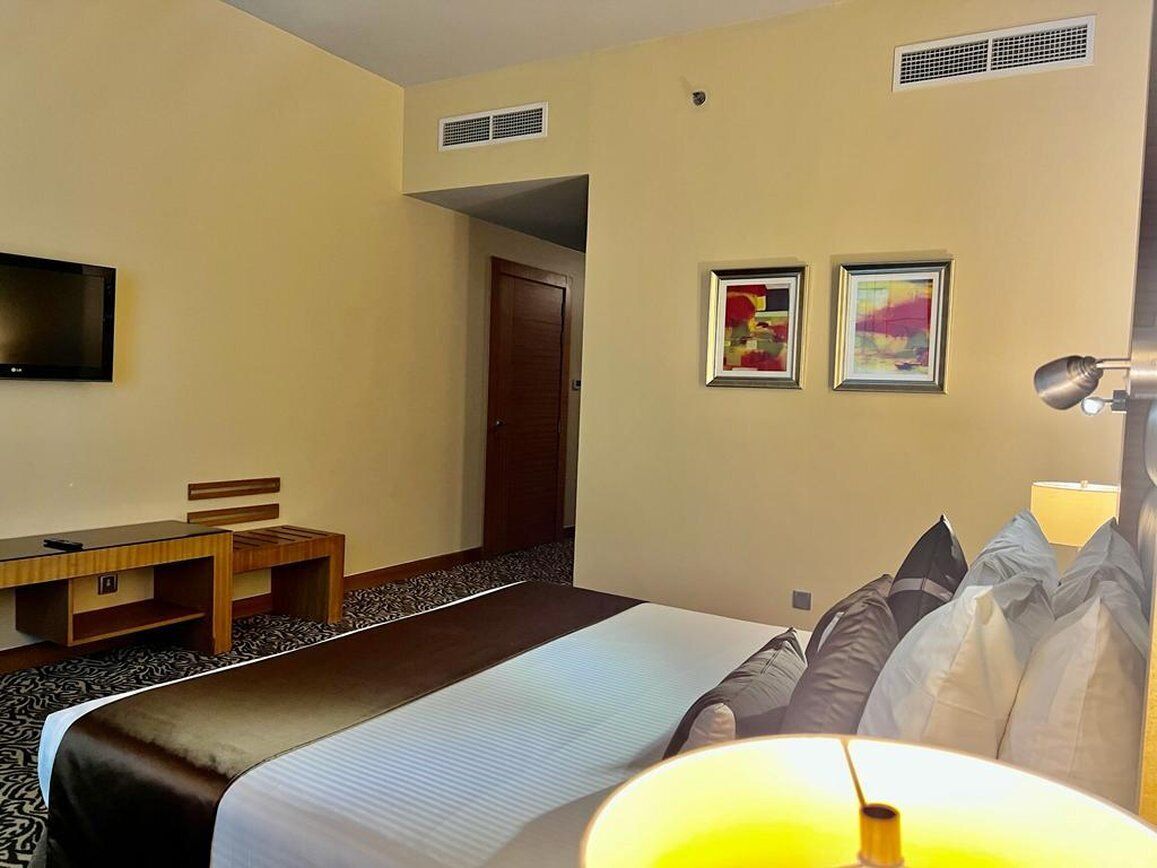 A hotel room with a bed, a desk, a TV, and two framed pictures on the wall.
