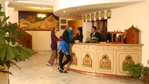 A reception area with a marble floor, a reception desk with a clock, and a Buddha statue. - Hotel Greenwich Village (Lalitpur)