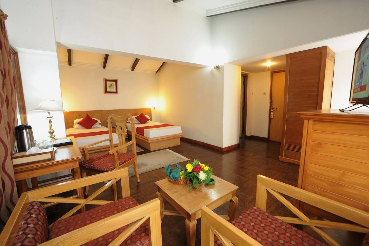 A cozy room with a bed, a desk, and a chair. There is a small table with a vase of flowers.