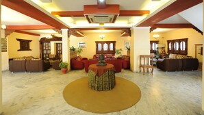A spacious living area with a central round table, sofas, and potted plants. - Hotel Greenwich Village (Lalitpur)