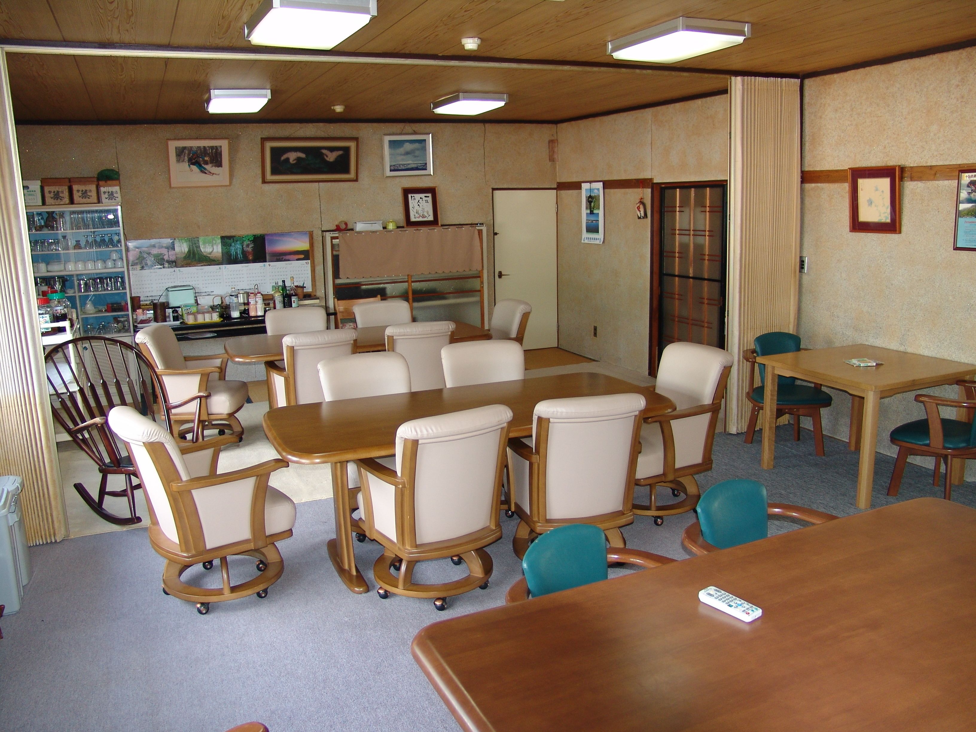 A conference room with a large table, several chairs, a small kitchenette, and a window with curtains.