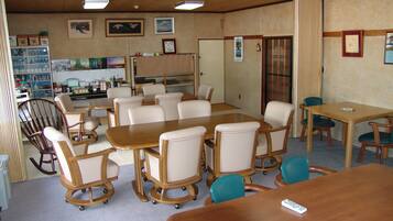 A conference room with a large table, several chairs, a small kitchenette, and a window with curtains.