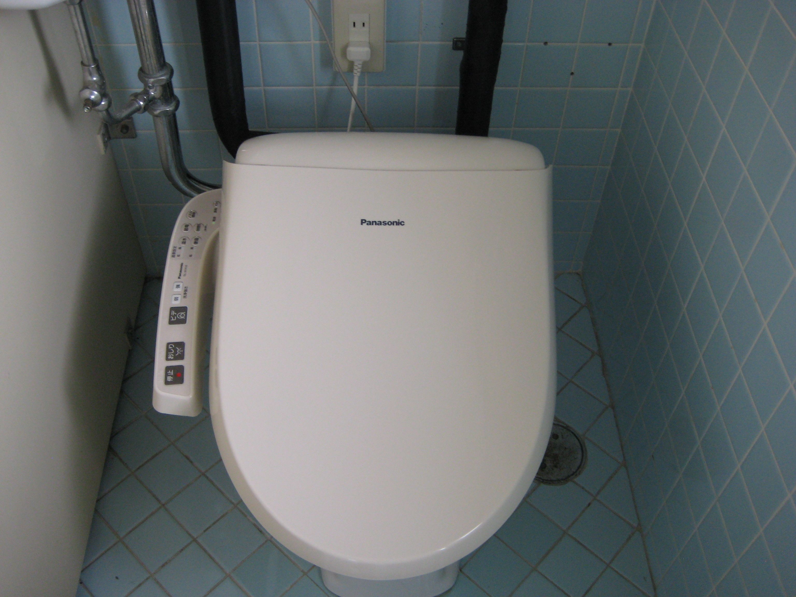 A white toilet with a control panel, a visible power outlet, and a tiled floor.