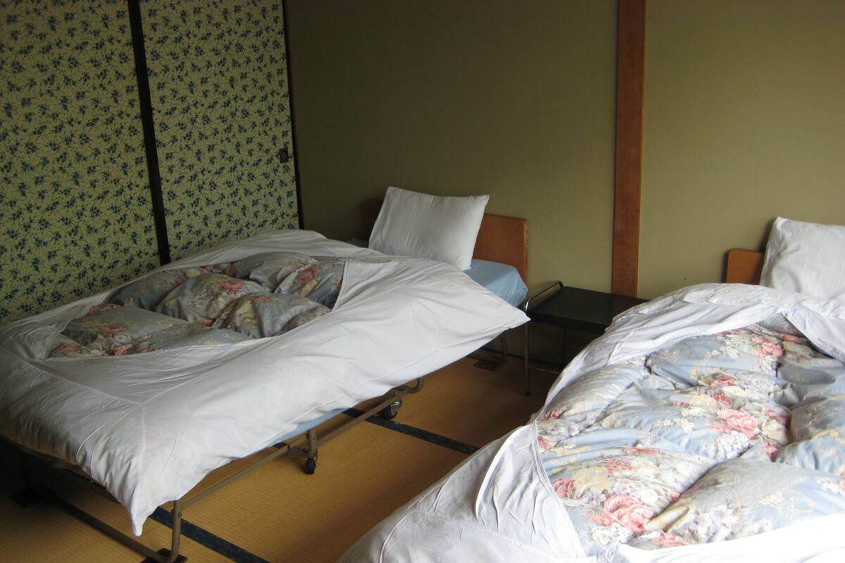 Una habitación con dos camas, cada una con ropa de cama floral y almohadas blancas. Hay una mesita entre las camas y el papel tapiz de las paredes presenta un estampado floral.